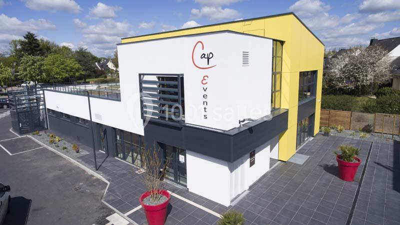 Bâtiment moderne avec façade blanche et jaune, grandes baies vitrées et logo ’Cap Events’ visible sur le mur.