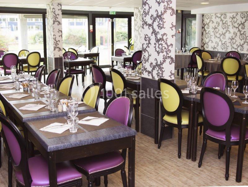 Salle de restaurant lumineuse avec tables dressées, chaises colorées violettes et jaunes, et décorations murales.