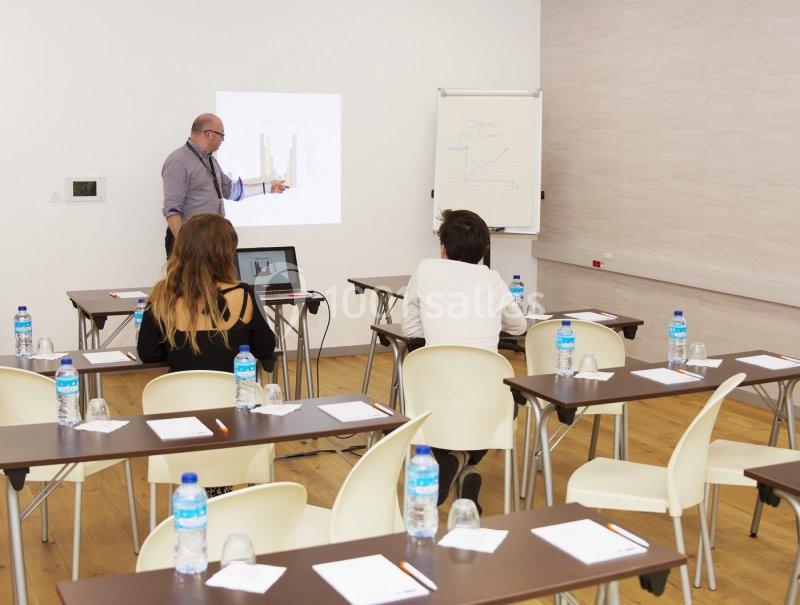 Un formateur présente des graphiques à trois participants dans une salle de réunion équipée de tables et chaises.