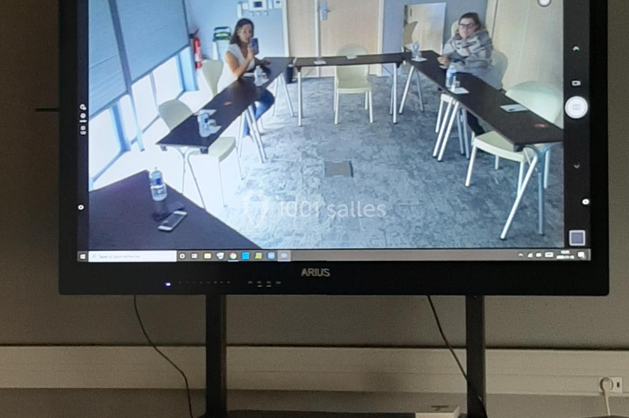 Écran affichant une visioconférence avec deux personnes assises à une table en salle de réunion.