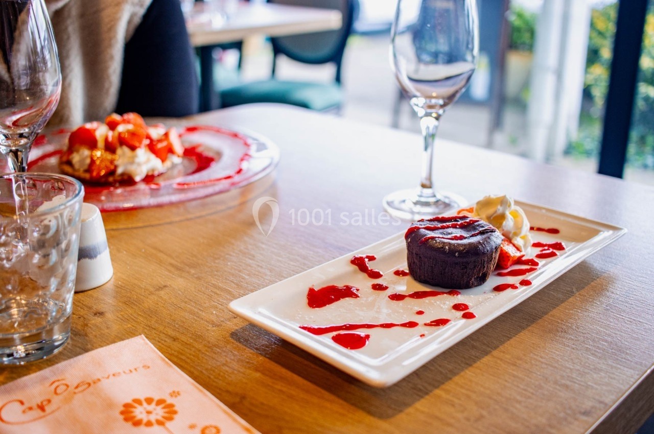 Dessert au chocolat avec coulis de fruits rouges et crème, servi sur une table de restaurant avec des verres vides.