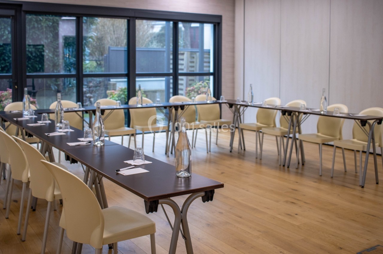 Salle de réunion lumineuse avec des tables disposées en U, des chaises beiges et des bouteilles d'eau sur les tables.