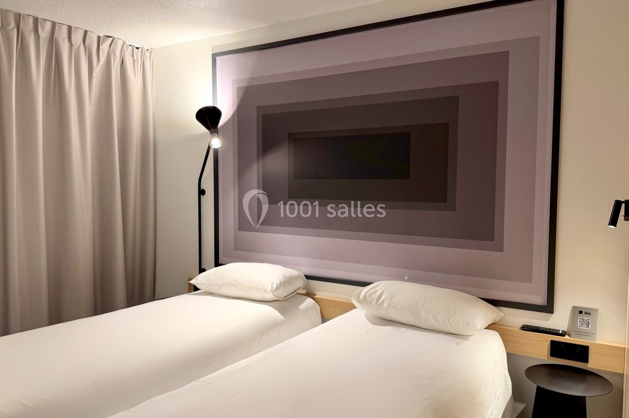 Deux lits simples avec une grande œuvre d'art géométrique en arrière-plan dans une chambre lumineuse.
