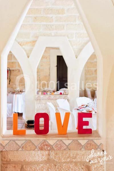Mot ’LOVE’ en lettres colorées posé sur un muret, avec une salle de réception lumineuse en arrière-plan.