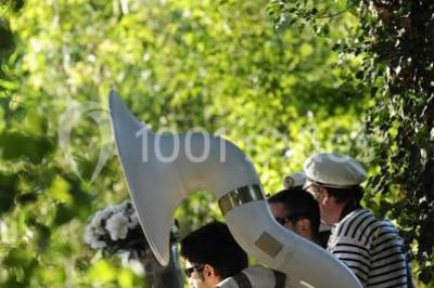 Des musiciens en tenue blanche et rayée jouent des percussions en extérieur, près d'une petite fille.