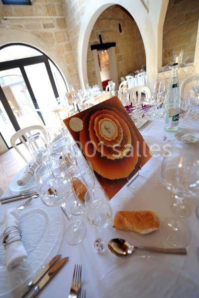 Table dressée pour un repas, avec vaisselle élégante, menu décoratif au centre et pain disposé sur la nappe.