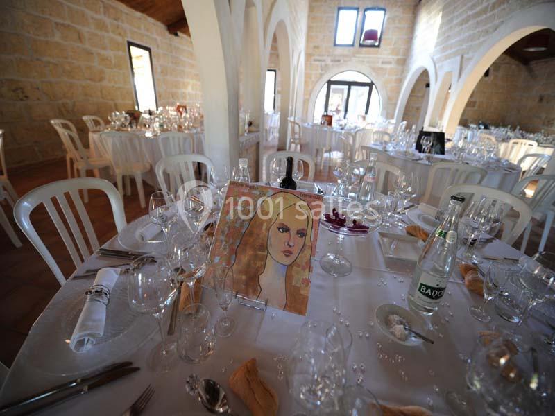 Salle de réception lumineuse avec tables dressées, décorées de verres, serviettes et une peinture en guise de centre de…