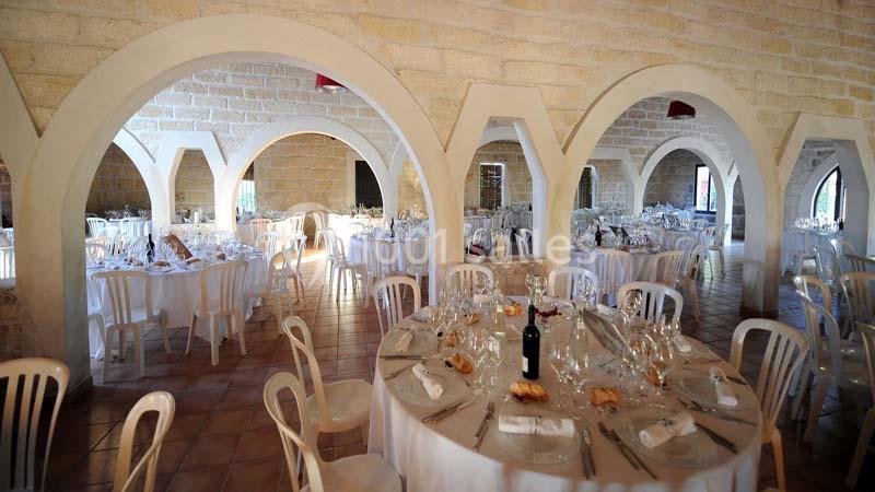 Salle de réception lumineuse avec tables rondes dressées, nappes blanches et chaises en plastique blanc.