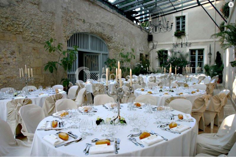 Salle de réception élégante avec tables rondes dressées, nappes blanches, chandeliers et décoration végétale.