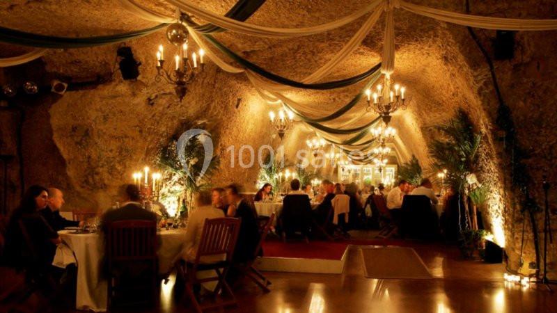 Salle de restaurant aménagée dans une grotte, éclairée par des chandeliers, avec des convives attablés.