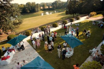 Façade d'un bâtiment ancien en pierre avec une piscine et un jardin arboré sous un ciel bleu.