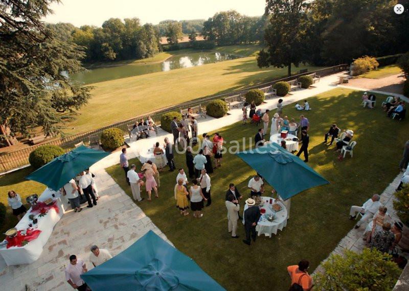 Personnes réunies dans un jardin lors d'un événement, avec des tables, des parasols et un paysage verdoyant en arrière-plan.