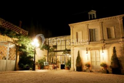 Façade d'un bâtiment ancien en pierre avec une piscine et un jardin arboré sous un ciel bleu.