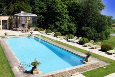 Façade d'un bâtiment ancien en pierre avec une piscine et un jardin arboré sous un ciel bleu.