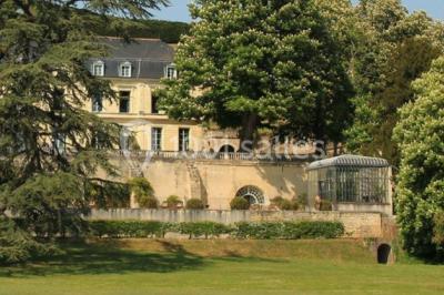 Façade d'un bâtiment ancien en pierre avec une piscine et un jardin arboré sous un ciel bleu.