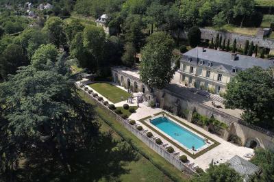 Façade d'un bâtiment ancien en pierre avec une piscine et un jardin arboré sous un ciel bleu.