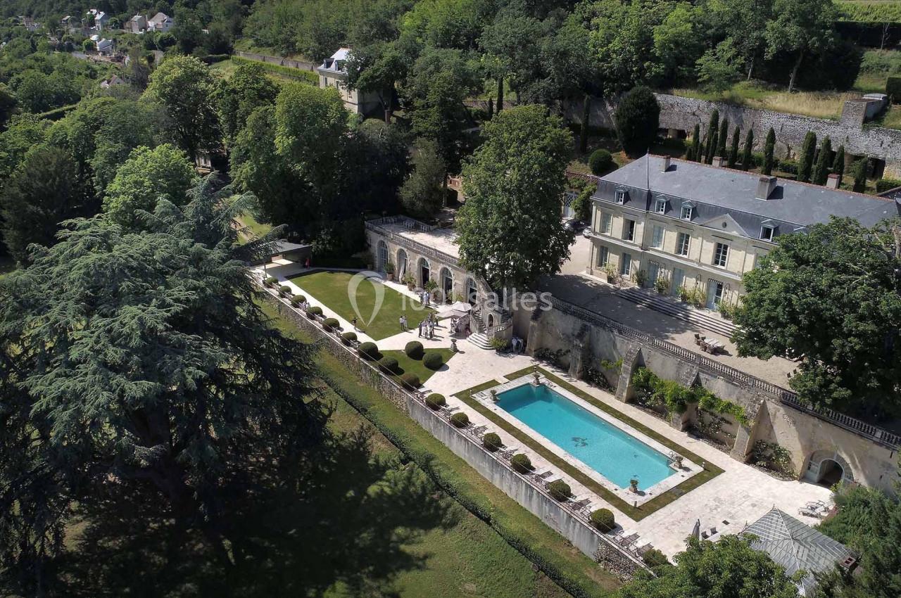 Vue aérienne d'une grande maison entourée de jardins, avec une piscine et des arbres dans un cadre verdoyant.