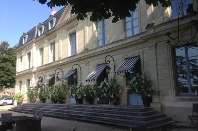 Façade d'un bâtiment ancien en pierre avec une piscine et un jardin arboré sous un ciel bleu.