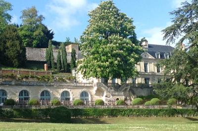 Façade d'un bâtiment ancien en pierre avec une piscine et un jardin arboré sous un ciel bleu.