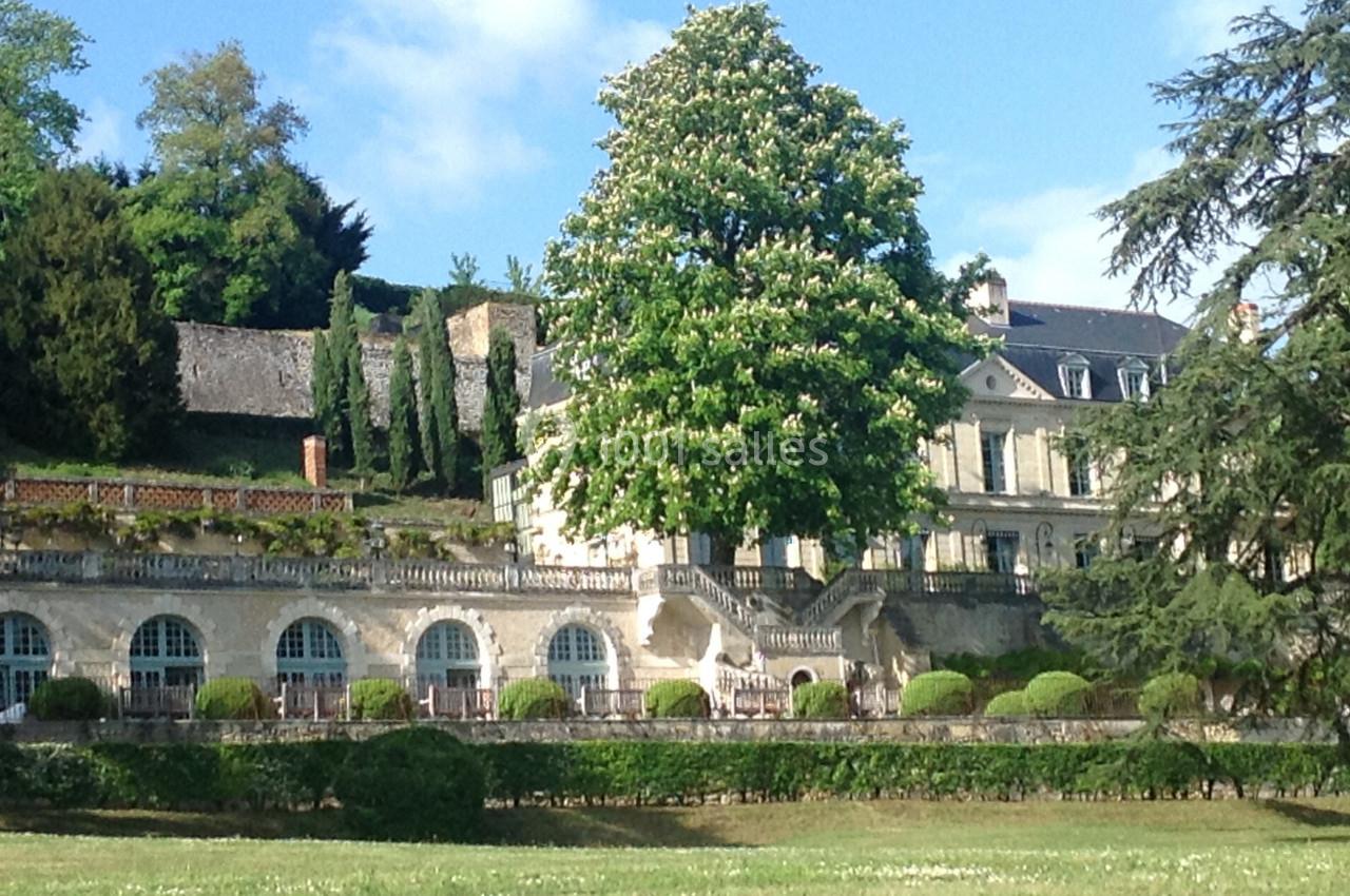 Demeure ancienne entourée de jardins, avec un grand arbre en fleurs au premier plan et un ciel dégagé.