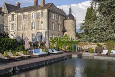 Piscine extérieure avec transats et parasols, entourée de verdure et située près d'une maison en pierre.