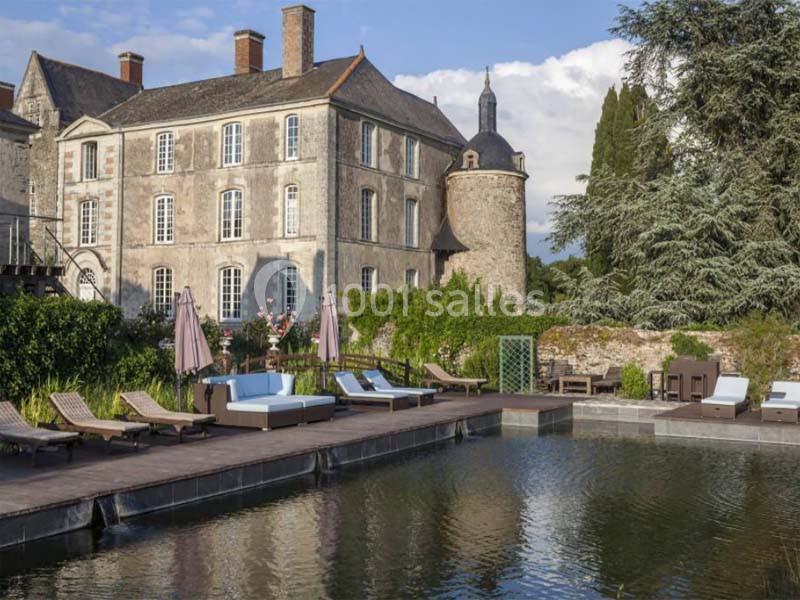 Château historique avec piscine, terrasse en bois, transats et végétation environnante.