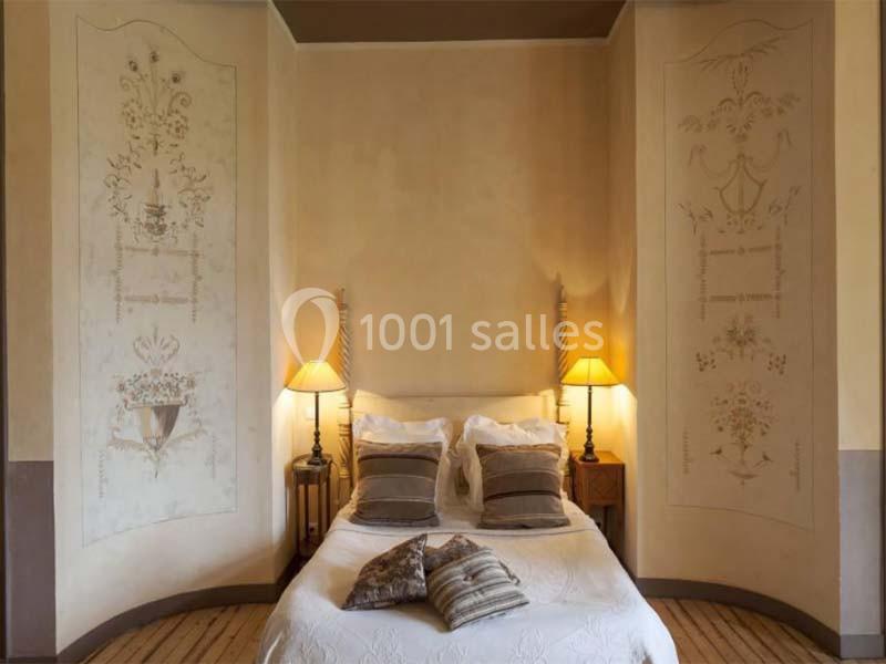 Lit double avec coussins et lampes de chevet, encadré par des murs décorés de motifs peints.