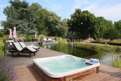 Piscine extérieure avec transats et parasols, entourée de verdure et située près d'une maison en pierre.