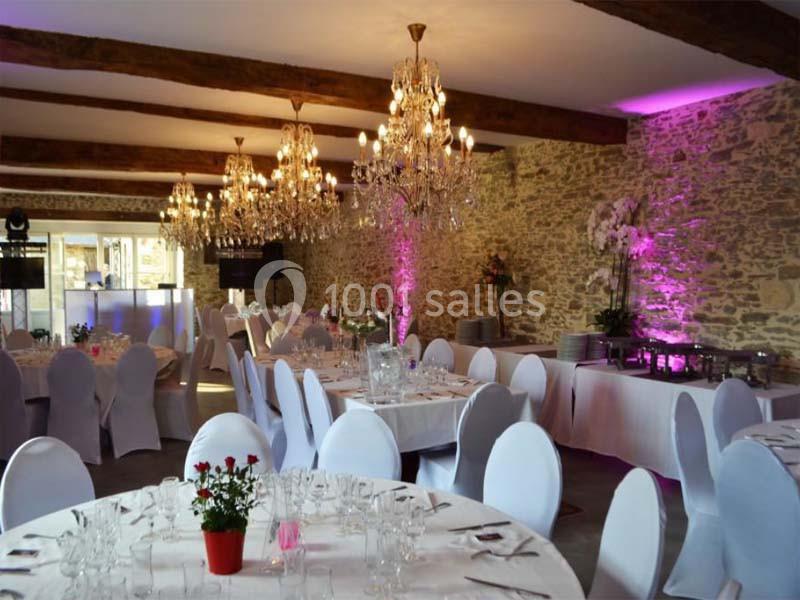 Salle de réception décorée avec des tables rondes dressées, des chaises blanches et des lustres suspendus.