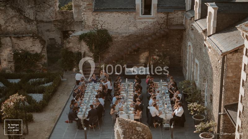 Groupe de personnes dînant à une longue table en extérieur, dans une cour entourée de bâtiments en pierre.