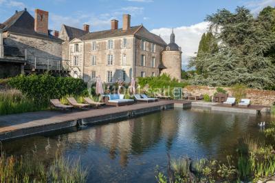 Piscine extérieure avec transats et parasols, entourée de verdure et située près d'une maison en pierre.