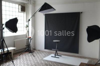 Exposition artistique dans une salle avec des œuvres colorées accrochées aux murs et des photos disposées sur une table.