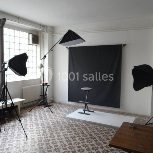 Studio photo avec fond noir, tabouret central, éclairage professionnel et sol en carreaux à motifs.