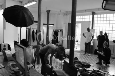 Exposition artistique dans une salle avec des œuvres colorées accrochées aux murs et des photos disposées sur une table.