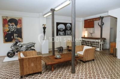 Exposition artistique dans une salle avec des œuvres colorées accrochées aux murs et des photos disposées sur une table.