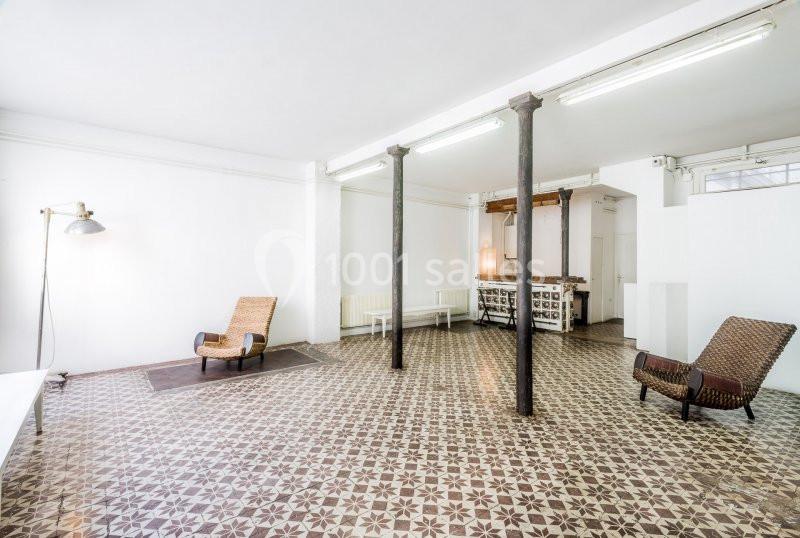 Espace intérieur lumineux avec carrelage à motifs, colonnes métalliques, fauteuils en osier et comptoir en arrière-plan.