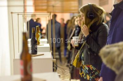 Exposition artistique dans une salle avec des œuvres colorées accrochées aux murs et des photos disposées sur une table.
