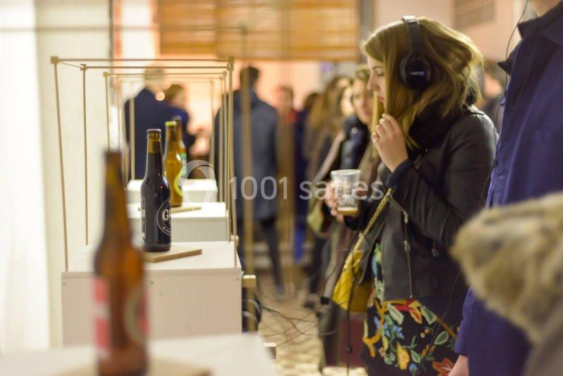 Une femme écoute un audio avec un casque près d'une exposition de bouteilles, dans un espace intérieur animé.