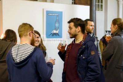 Exposition artistique dans une salle avec des œuvres colorées accrochées aux murs et des photos disposées sur une table.