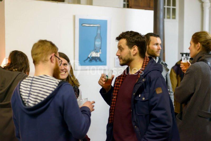 Des personnes discutent et boivent dans un espace intérieur, avec un tableau bleu accroché au mur en arrière-plan.