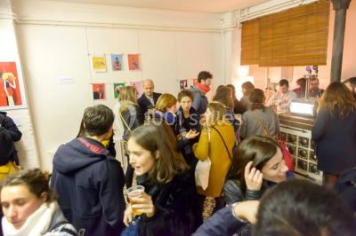Exposition artistique dans une salle avec des œuvres colorées accrochées aux murs et des photos disposées sur une table.