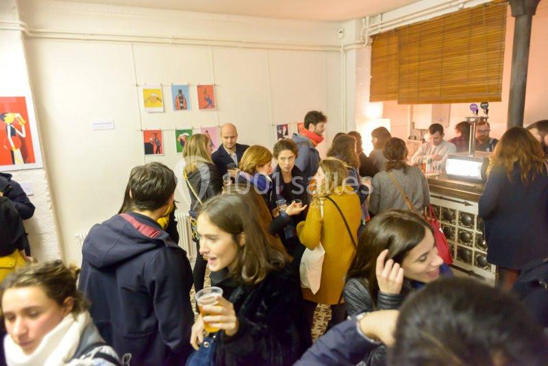 Groupe de personnes discutant et partageant des boissons dans une petite galerie d'art éclairée.