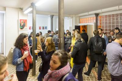 Exposition artistique dans une salle avec des œuvres colorées accrochées aux murs et des photos disposées sur une table.