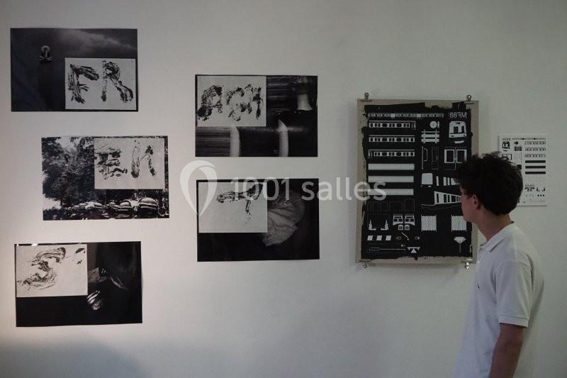 Un homme observe des œuvres en noir et blanc accrochées sur un mur blanc dans une exposition.