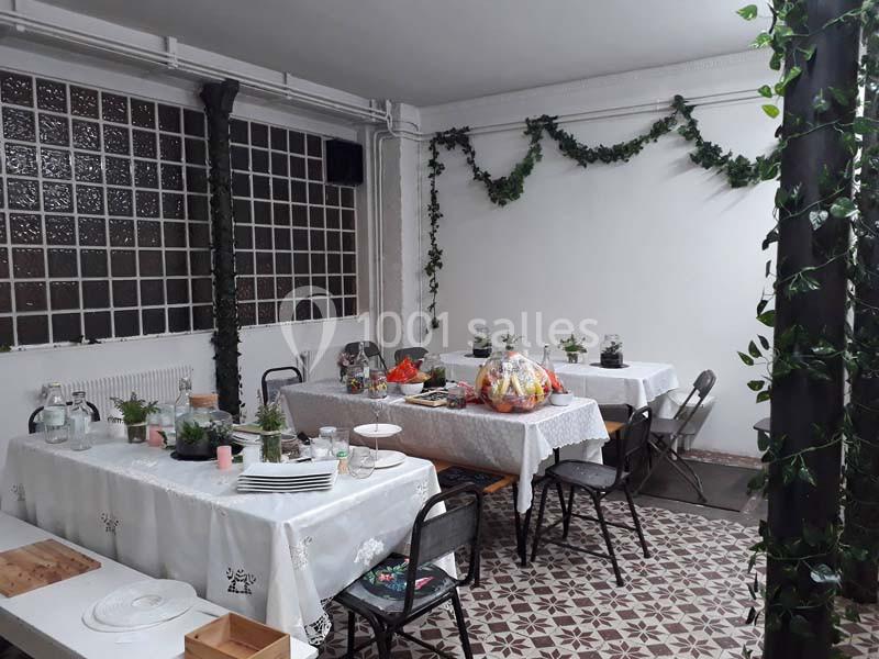 Salle décorée avec des guirlandes végétales, tables dressées avec nappes blanches, plantes et accessoires de réception.