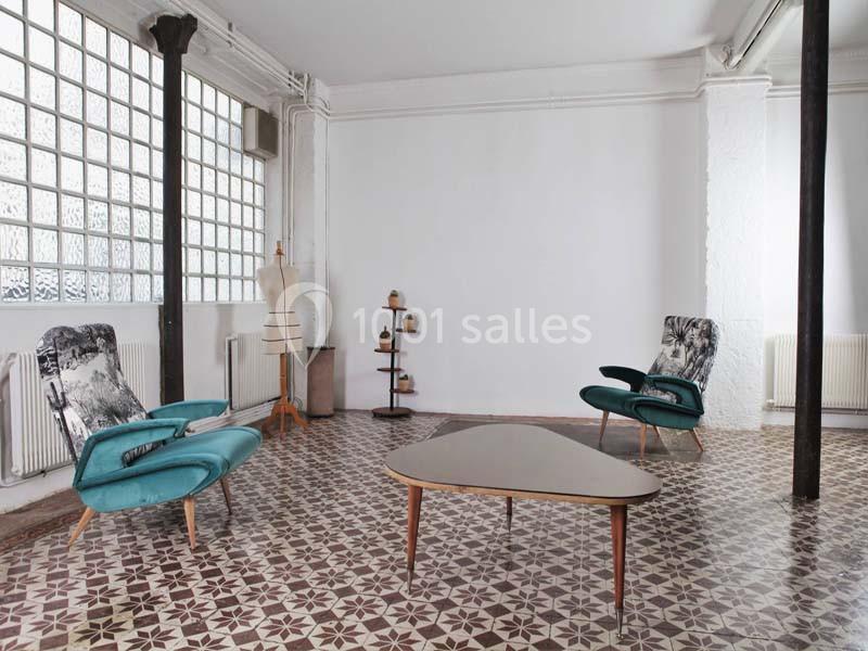 Salle lumineuse avec carrelage géométrique, fauteuils vintage, table basse triangulaire et mannequin de couture.