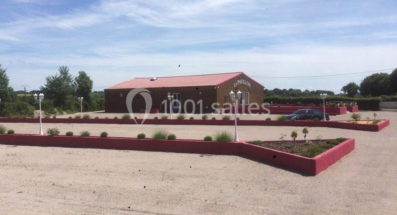 Bâtiment en briques rouges entouré d'un parking et de parterres de fleurs, sous un ciel dégagé.