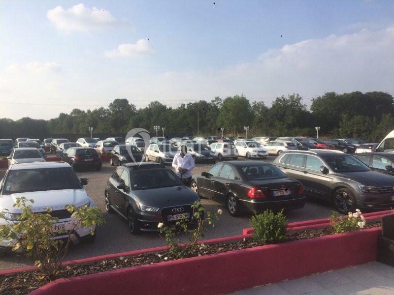 Parking extérieur rempli de voitures, avec un homme debout près d'une Audi noire sous un ciel dégagé.