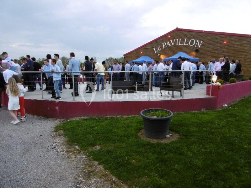 Groupe de personnes rassemblées sur une terrasse devant un bâtiment nommé ’Le Pavillon’ par temps nuageux.