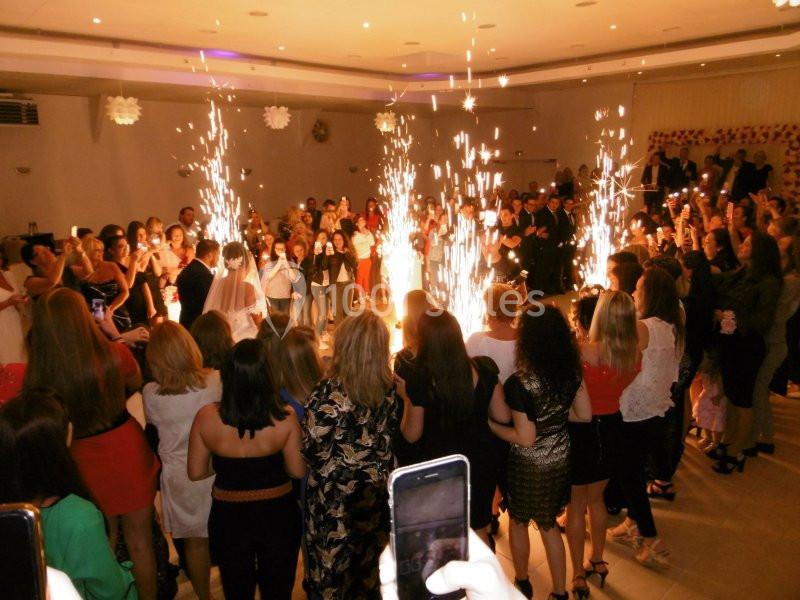 Groupe de personnes entourant un couple dansant au centre d'une salle, avec des étincelles pyrotechniques.